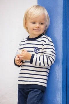 jeune garçon qui se tient sur un mur avec pull rayé